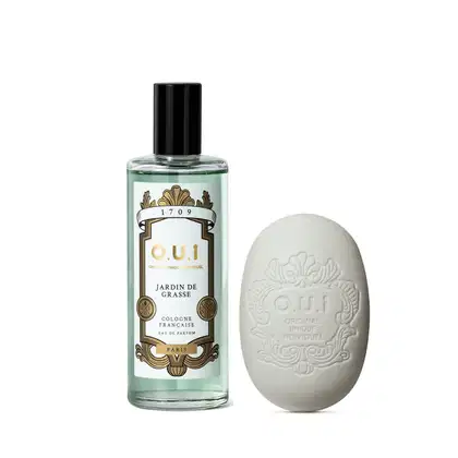 Frasco de perfume O.U.i. Jardin de Grasse com rótulo dourado e verde, e sabonete em forma de ovo com logotipo em relevo. Produtos da marca francesa O.U.i. com design elegante e sofisticado.