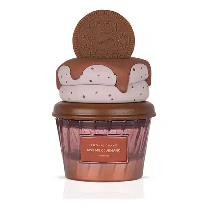 Frasco de perfume da marca Lattafa em formato de cupcake, com tampa em formato de biscoito. Embalagem em tons de marrom e rosa, com rótulo indicando o nome "Cookie Crave" e a frase "Give me gourmand".