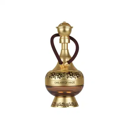 Frasco de perfume dourado com detalhes florais em relevo, contendo o nome "Dream of Haze" em sua base. O frasco possui um design elegante e retrátil, com um cordão marrom escuro.