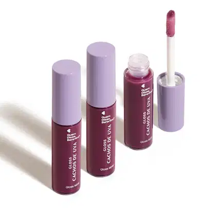 Imagem de combo com três frascos de 10ml contendo gloss labial Cachos de Uva QDB E Cuide-se Bem Quem Disse, Berenice?. A embalagem é transparente com conteúdo roxo, tampa cinza e aplicador macio na cor roxa. O fundo é branco com leve sombreado.