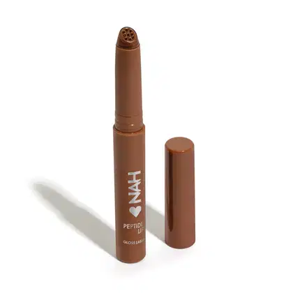 Produto de beleza Nah Cardoso em formato de batom, com embalagem marrom e rótulo com o nome "NAH" e "PEPTIDE LIP GLOSS LABEL". O produto possui formato cilíndrico e tampa removível.