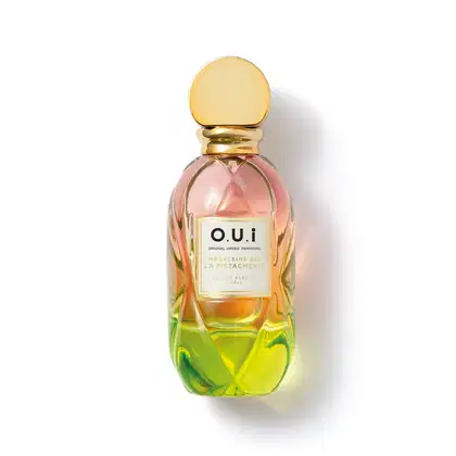 Frasco de perfume O.U.i. com design escultural em tons de rosa, amarelo e verde. Rótulo com nome da marca e informações sobre a fragrância "Madeleine 922 La Pistacherie".