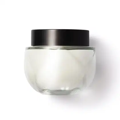 Frasco de vidro arredondado, transparente com tampa preta de rosquear, contendo o creme na cor branca. Design minimalista e elegante.