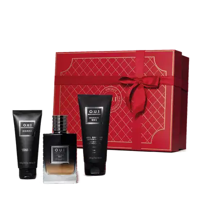 Conjunto. No centro, frasco de vidro contendo líquido da fragrância em degradê de preto à âmbar, de alto a baixo. Ao lado, tubo preto de gel de banho e um tubo preto de creme de barbear. Acompanha caixa vermelha com detalhes em dourado e laço vermelho.