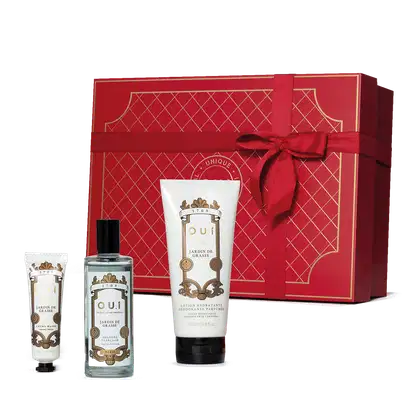 Conjunto. Frasco de colônia transparente com líquido azul claro e detalhes dourados no rótulo branco, um frasco de loção para mãos branco em forma de bisnaga e um tubo branco de loção hidratante. Todos com rótulo barroco com letras douradas e pretas.