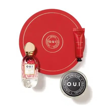Conjunto inclui um frasco de perfume de vidro com tampa dourada, uma caixa vermelha com o logotipo da marca, e um tubo de creme para as mãos também com o logotipo. Todos os itens apresentam design elegante e cores predominantemente vermelhas e douradas.