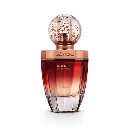 Frasco de vidro arredondado com textura hexagonal, cor degradê cobre escuro. Tampa de vidro redonda com detalhes de confetes na cor bronze rosado. Rótulo no topo e na base com o nome do produto e marca em letras douradas sobre o fundo rosado do líquido.