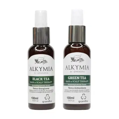 Dois frascos de produtos de cabelo e couro cabeludo da marca Alkymia di Grandha, com rótulos em preto e branco. Um frasco contém "Black Tea Hair & Scalp Therapy" e o outro "Green Tea Hair & Scalp Therapy", ambos com 130ml.
