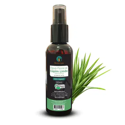 A imagem mostra um frasco de plástico ambar com tampa em spray da Água Floral de Capim Limão da marca Oleoterapia Brasil. O frasco contém 120ml. Ao lado do frasco, há folhas verdes de capim limão.