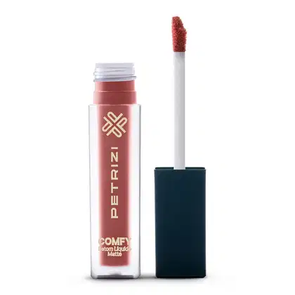A imagem mostra o produto Petrizi Makeup Comfy, um batom líquido matte em embalagem plástica transparente com tampa preta e aplicador em formato de pincel, na cor nude rosado