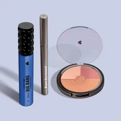 Máscara de cílios Big Bang 360° em embalagem azul com tampa preta, lápis de olhos em embalagem cinza e mini paleta de maquiagem em estojo preto e tampa transparente, todos da marca Quem Disse, Berenice? em fundo azul claro.