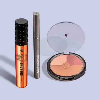 Máscara de cílios Big Bang 360° em embalagem laranja metalizada com tampa preta texturizada de corações, lápis retrátil em embalagem cinza e mini paleta de maquiagem em embalagem preta com tampa transparente, todo Quem Disse, Berenice? em fundo azul.
