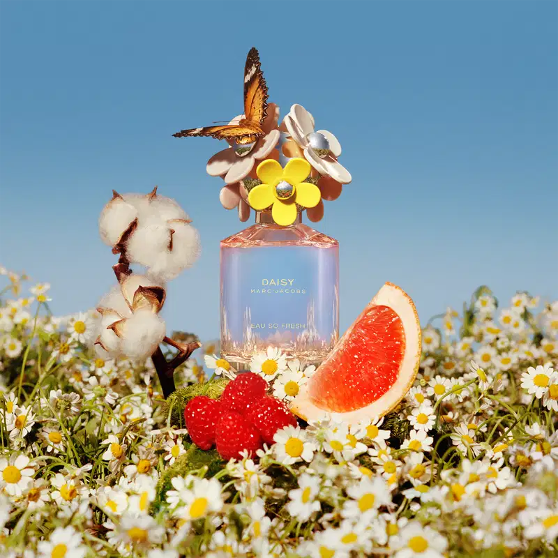Frasco de perfume Daisy Marc Jacobs Eau So Fresh, com tampa decorada com flores coloridas em tons de rosa, amarelo e branco, em fundo branco.