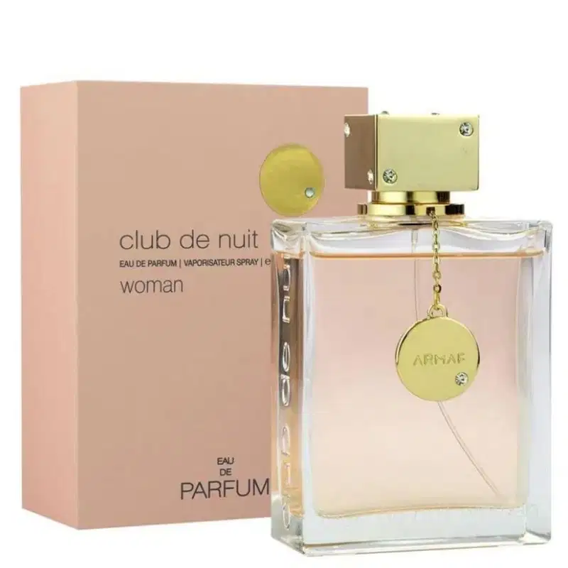 Frasco de perfume feminino da marca Armaf, chamado "Club de Nuit Woman", com embalagem rosa clara e detalhes dourados. O frasco possui um pingente dourado com o logotipo da marca.