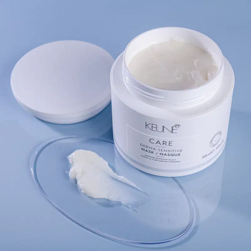 O produto de beleza Keune Care é um pote branco contendo uma máscara para cabelos sensíveis. O rótulo indica que o produto é uma máscara dermatologicamente sensível que acalma o couro cabeludo.