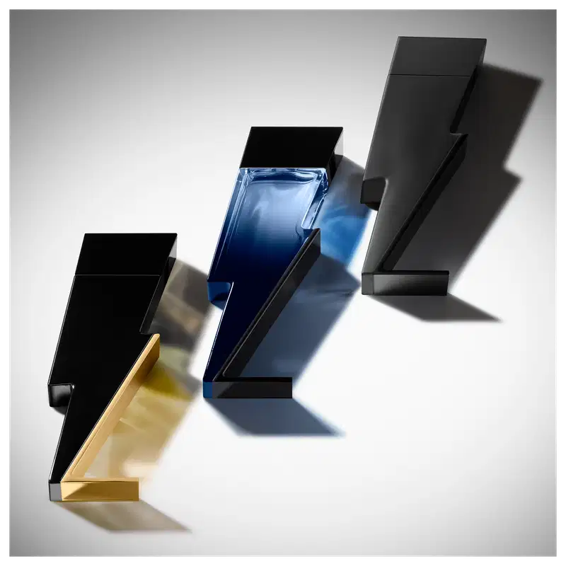 Três frascos de perfume Carolina Herrera em diferentes formatos e cores - azul, dourado e preto. As embalagens possuem design geométrico e minimalista, com destaque para os contornos angulares e a iluminação que cria sombras contrastantes.
