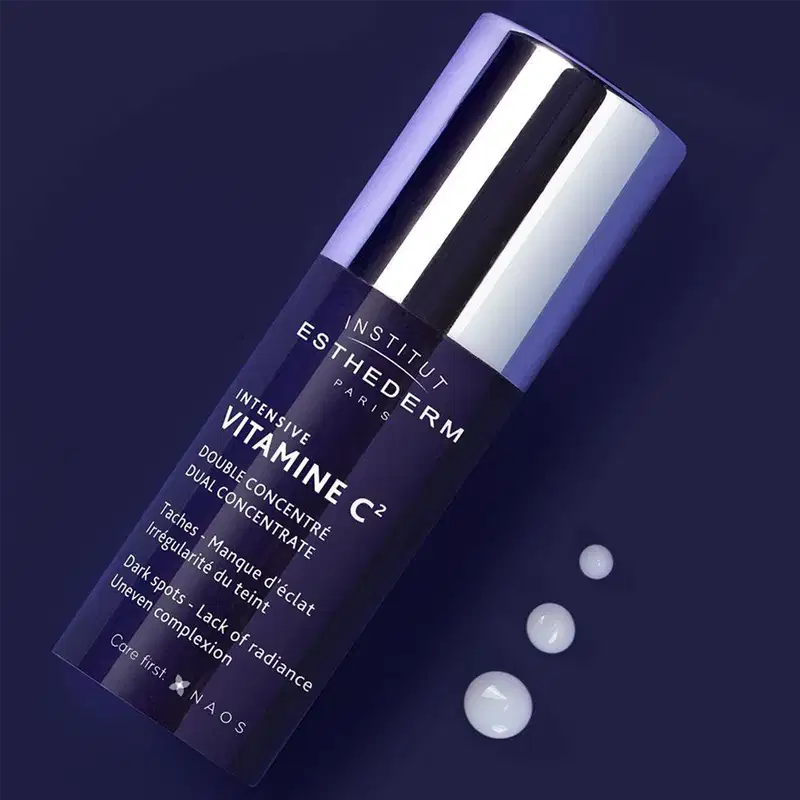 Embalagem de produto de beleza da marca Esthederm, com frasco de vidro escuro e tampa prateada, em fundo azul escuro com pequenas esferas brancas, sugerindo um ambiente sofisticado e de cuidados com a pele.