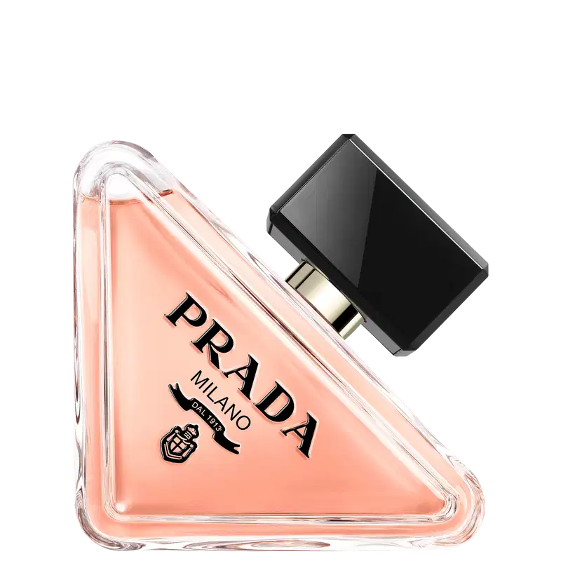 Frasco de perfume Prada com design triangular em vidro transparente, contendo líquido de cor rosa clara. O rótulo preto destaca o nome da marca "PRADA" em letras brancas.