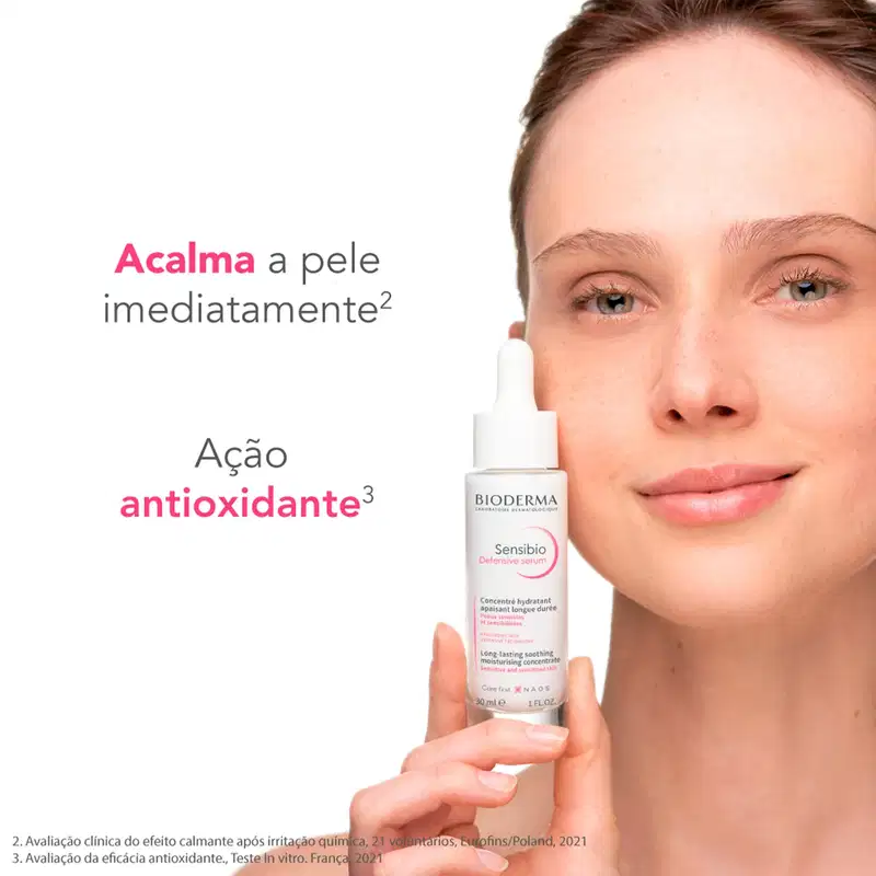 Uma mulher segurando um frasco de soro facial da marca Bioderma, com texto em português informando "Acalma a pele imediatamente" e "Ação antioxidante".