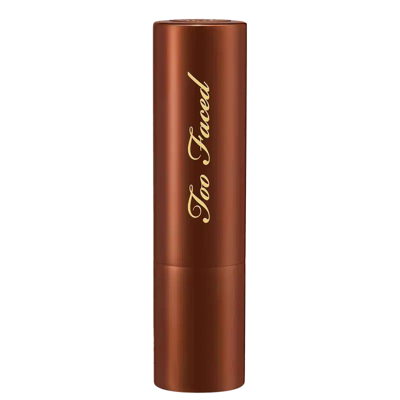 Bronzer em Bastão cilíndrico de metal cor marrom. O frasco tem uma tampa arredondada da mesma cor. O nome da marca "Too Faced" está escrito em letras douradas cursivas no corpo do frasco. O produto tem um acabamento metálico brilhante.