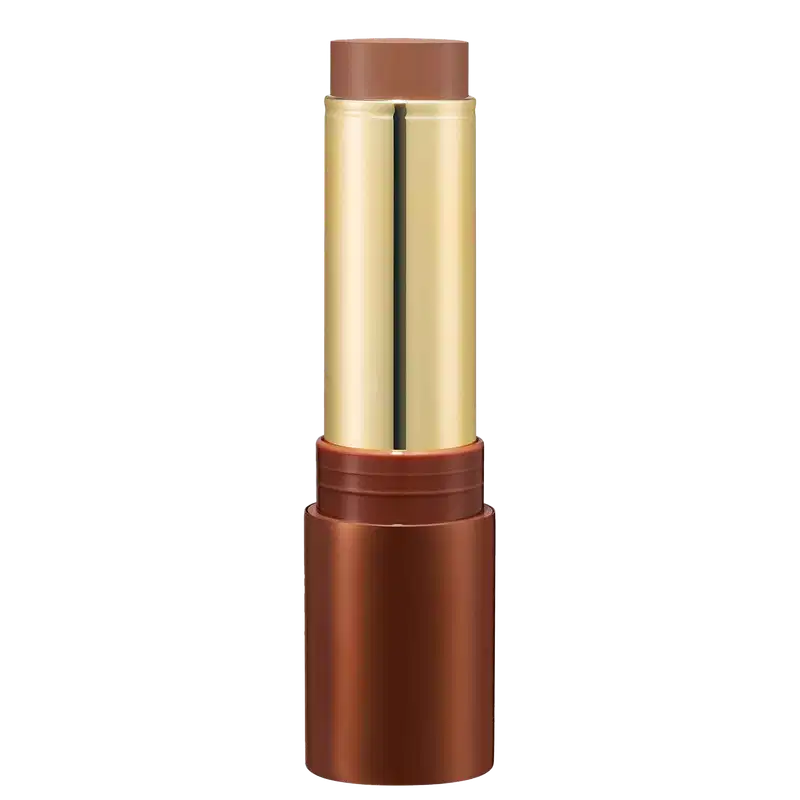Bronzer em Bastão em embalagem cilíndrica. O estojo é de metal dourado com detalhes em tom de marrom. A parte superior e inferior são de cor cobre fosco. A embalagem tem um design elegante e sofisticado.
