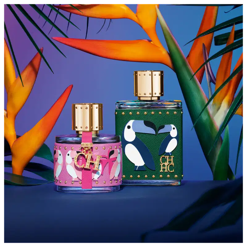 A imagem mostra dois frascos de perfume da marca Carolina Herrera, do lado esquerdo, um frasco pequeno, arredondado, com capa rosa com estampas de pássaros rosa e detalhes dourados. Do lado direito, o frasco de CH Men Birds of Paradise.