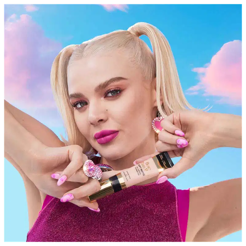 A imagem mostra uma mulher super produzida segurando uma embalagem da base próxima ao queixo.