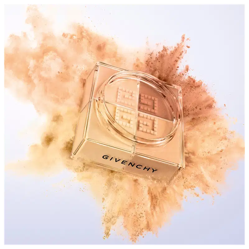 A imagem mostra a embalagem do pó solto e ao redor tem uma explosão das cores do pó, representando o poder e arte de givenchy.