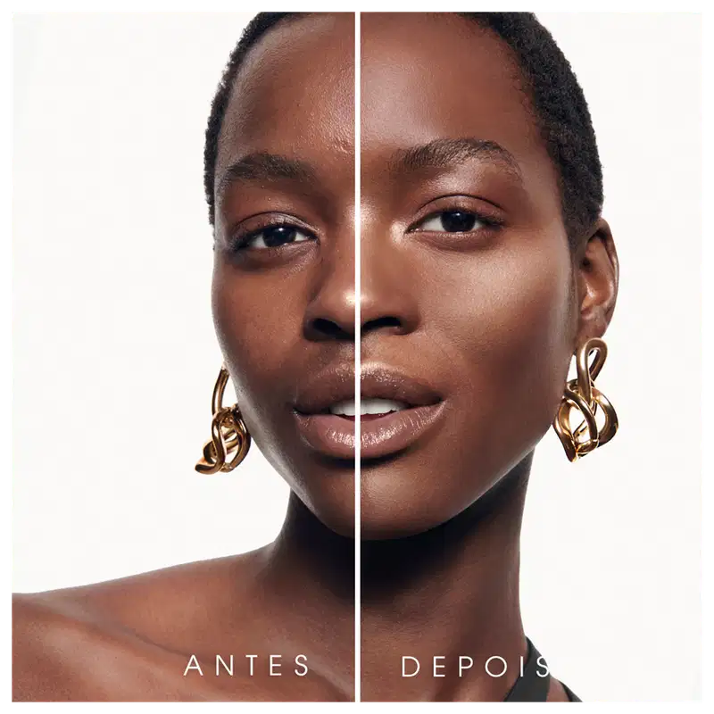 Esta imagem apresenta uma comparação antes e depois do uso do iluminador.  Na parte do "Antes" temos uma uma mulher de pele negra com algumas imperfeições. Na parte "Depois", a mesma mulher é retratada com uma pele mais uniforme e brilhante.