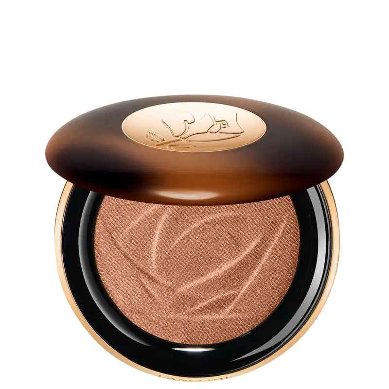 A imagem mostra o sérum iluminador Lancôme. A embalagem é redonda com tampa marrom e logotipo dourado no centro. A parte inferior preta com aro dourado. Interior contém o pó iluminador marrom com padrão rendado.