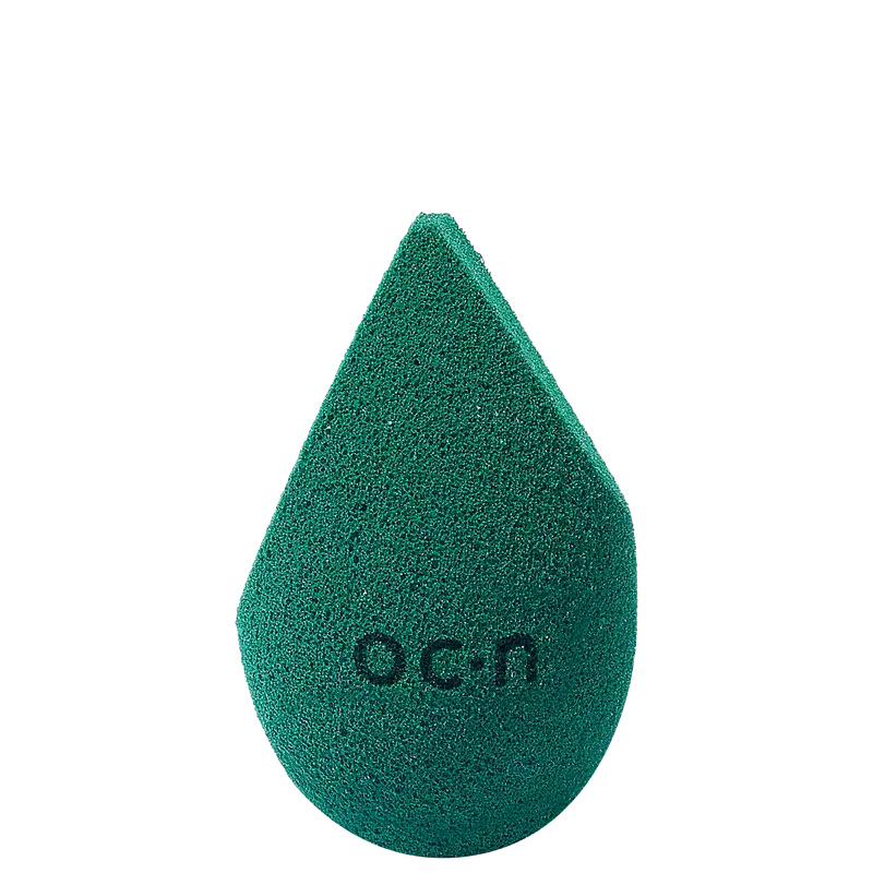 Esponja de maquiagem verde escuro com textura aveludada. Formato de gota com a palavra "Océane" impressa em relevo na superfície.