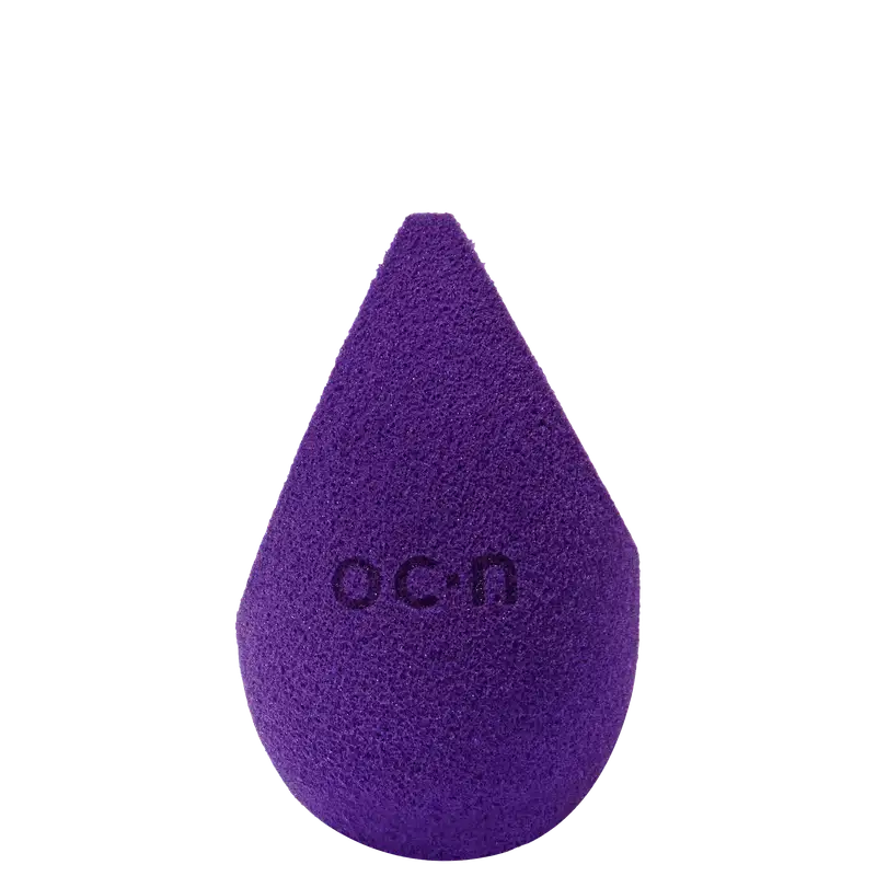 Esponja de maquiagem roxo escuro com textura aveludada. Formato de gota com a palavra "Océane" impressa em relevo na superfície.