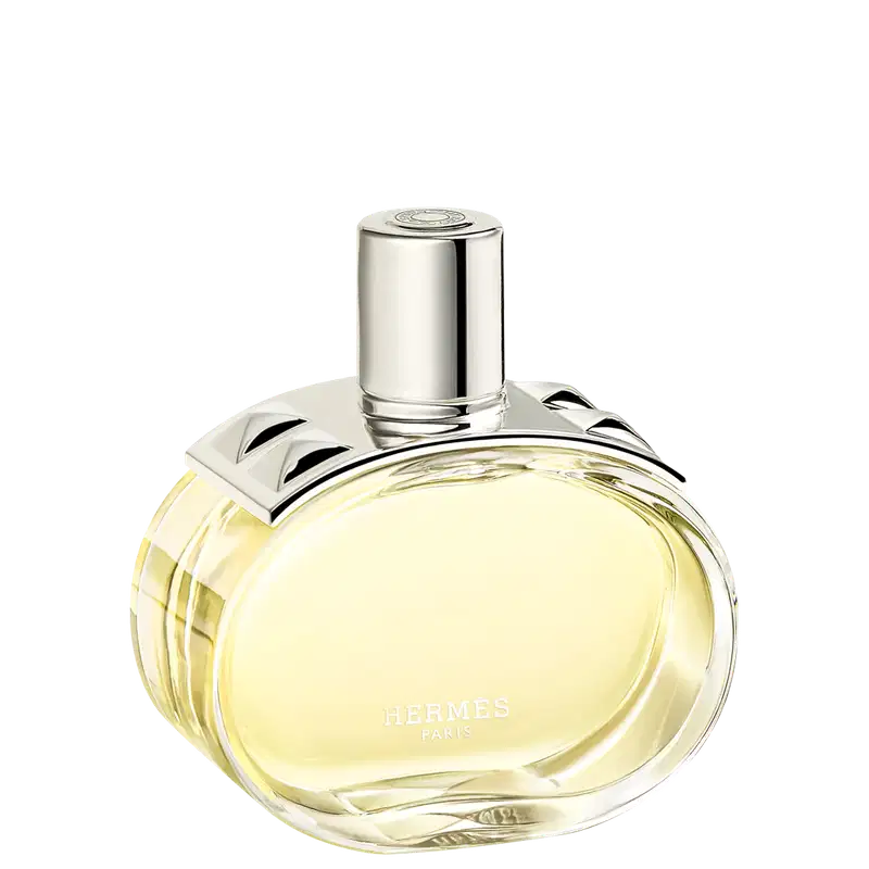 A imagem mostra o perfume Barénia de Hermès. Seu frasco é de vidro arredondado e transparente, permitindo ver o líquido amarelado em seu interior. Sua tampa é cilíndrica e prateada e possui uma aplicação com pinos em forma de pirâmide com facetas curvas.