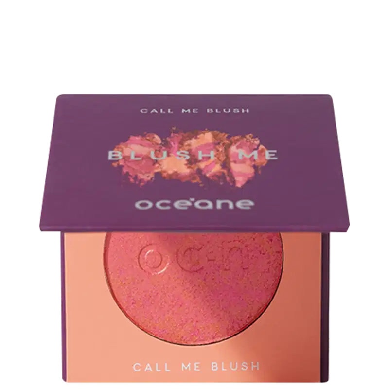 A imagem mostra o produto Blush Me da marca Océane. É uma embalagem quadrada de cor roxa que está semiaberta mostrando a cor do blush em um tom laranja com leve brilho perolado. A parte interna da embalagem é de cor pêssego claro,