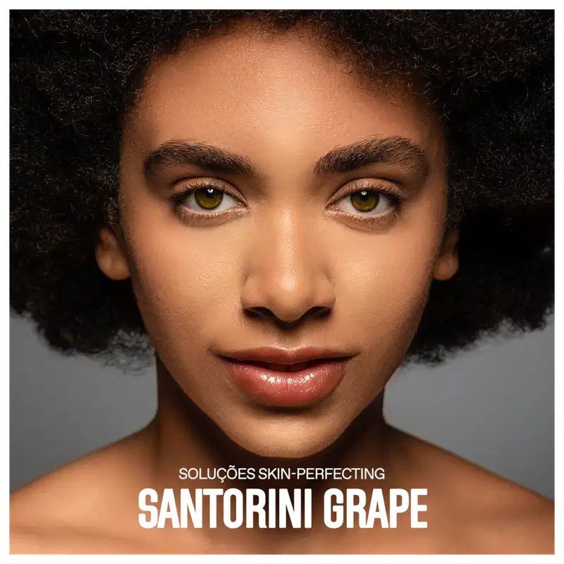 A imagem mostra um close-up do rosto de uma mulher negra com cabelos crespos e curtos. Ela tem olhos amendoados de cor amarelo-esverdeada. Sua pele tem um aspecto aveludado e uniforme, provavelmente resultado do uso dos produtos anunciados.