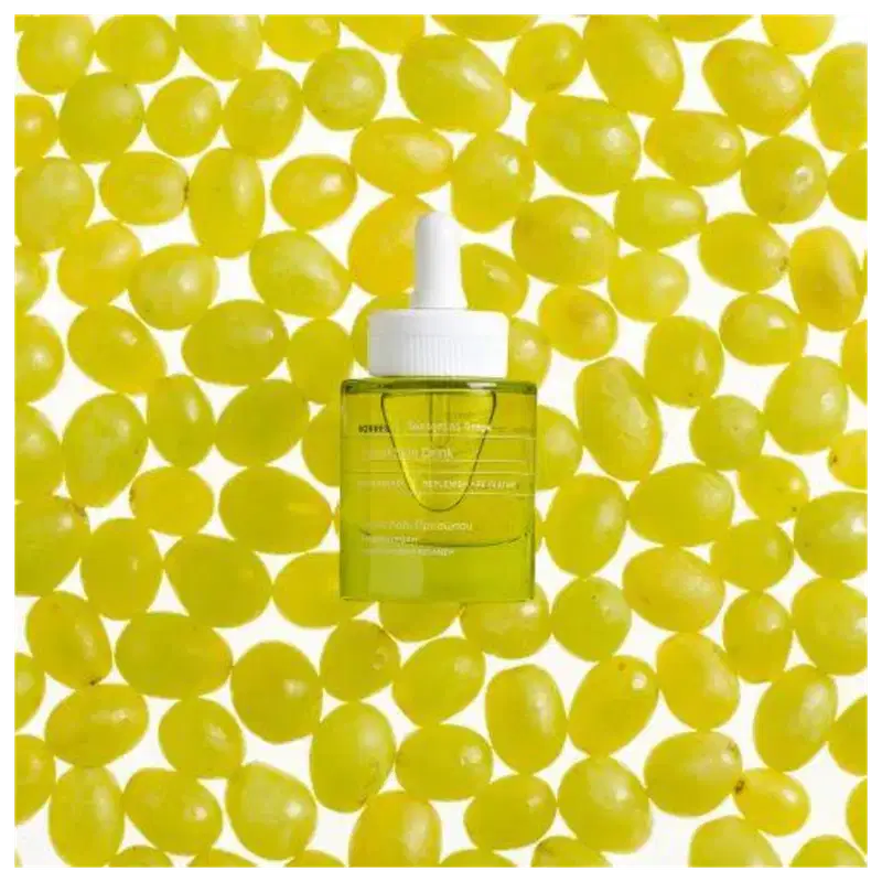 A imagem mostra o frasco do sérum rodeado de uvas verdes.