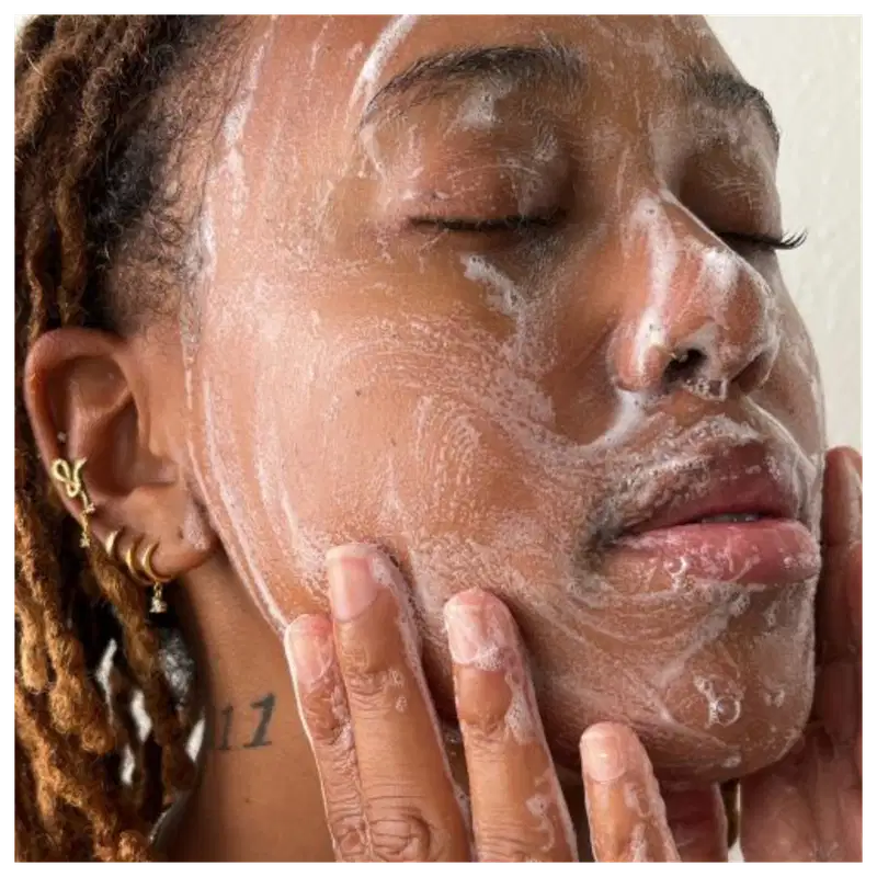 A imagem retrata um close-up do rosto de uma pessoa com pele negra aplicando a espuma sobre toda a face.