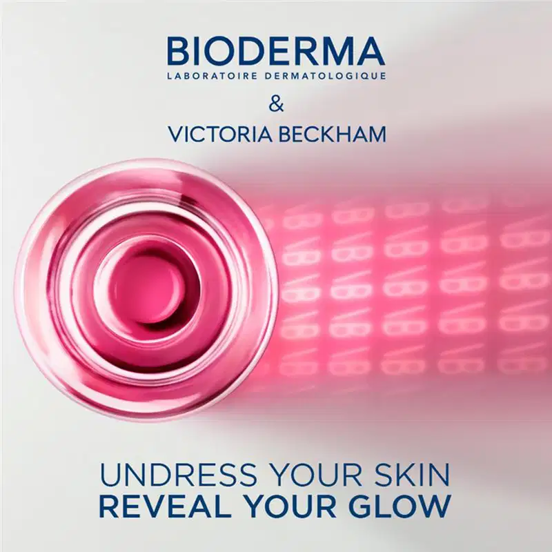 Embalagem rosa com texto "BIODERMA LABORATOIRE DERMATOLOGIQUE" e "VICTORIA BECKHAM". Recipiente com líquido rosa brilhante. Texto abaixo diz "UNDRESS YOUR SKIN REVEAL YOUR GLOW".