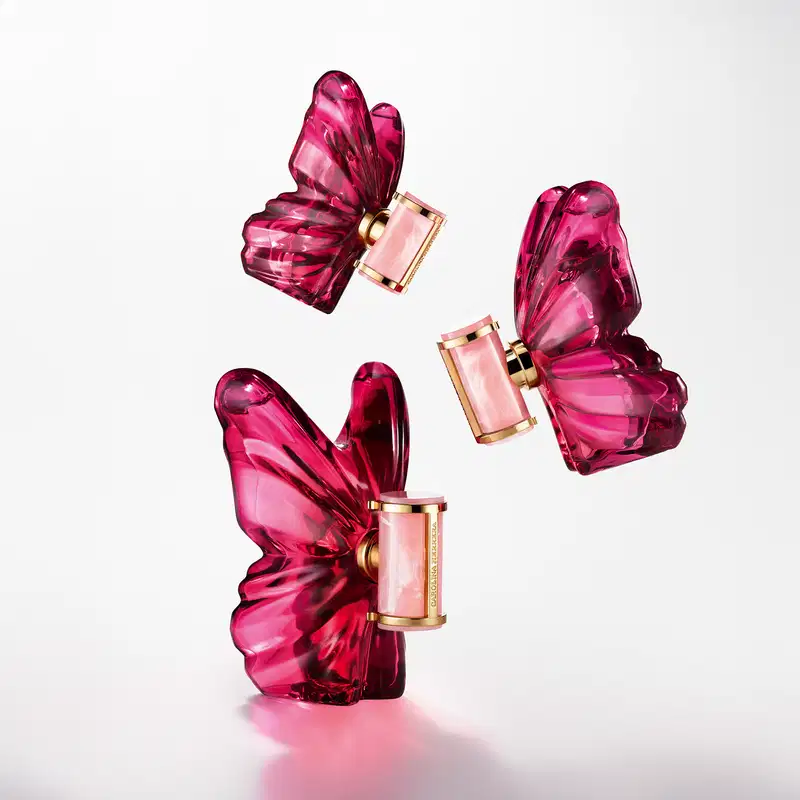 Frasco de perfume Carolina Herrera em formato escultural e vibrante na cor rosa, com rótulo dourado destacado contra fundo preto.