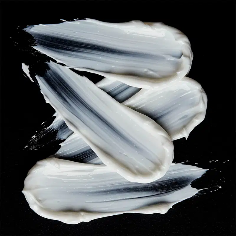 A textura do produto apresenta uma aparência cremosa e sedosa, com camadas de branco e cinza escuro que se misturam de forma fluida e dinâmica, criando uma sensação de movimento e profundidade.