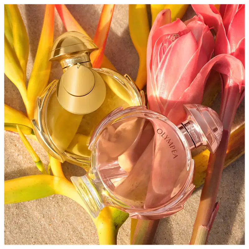 Dois itens de perfumaria em embalagens dourada e rosa, rodeados por flores de tulipa rosa e amarela, em um cenário com tons quentes e vibrantes, sugerindo um ambiente de beleza e elegância.