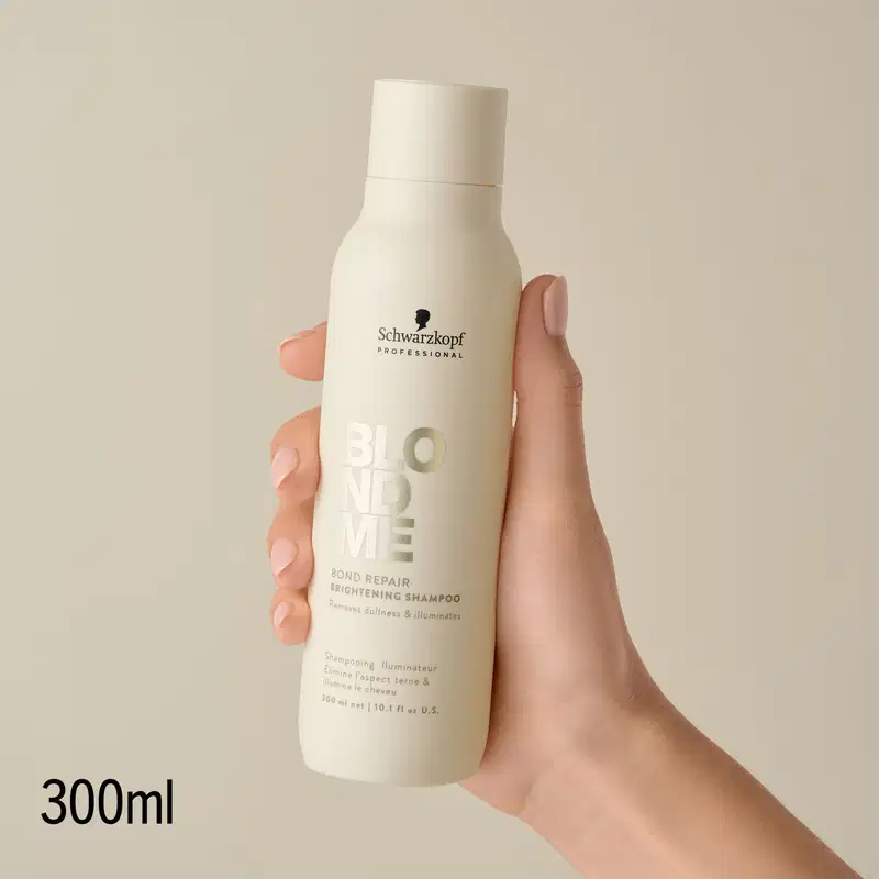 Produto de cabelo da marca Schwarzkopf Professional, em embalagem branca com detalhes em tons de cinza, em mãos femininas com unhas pintadas, em ambiente claro e neutro.