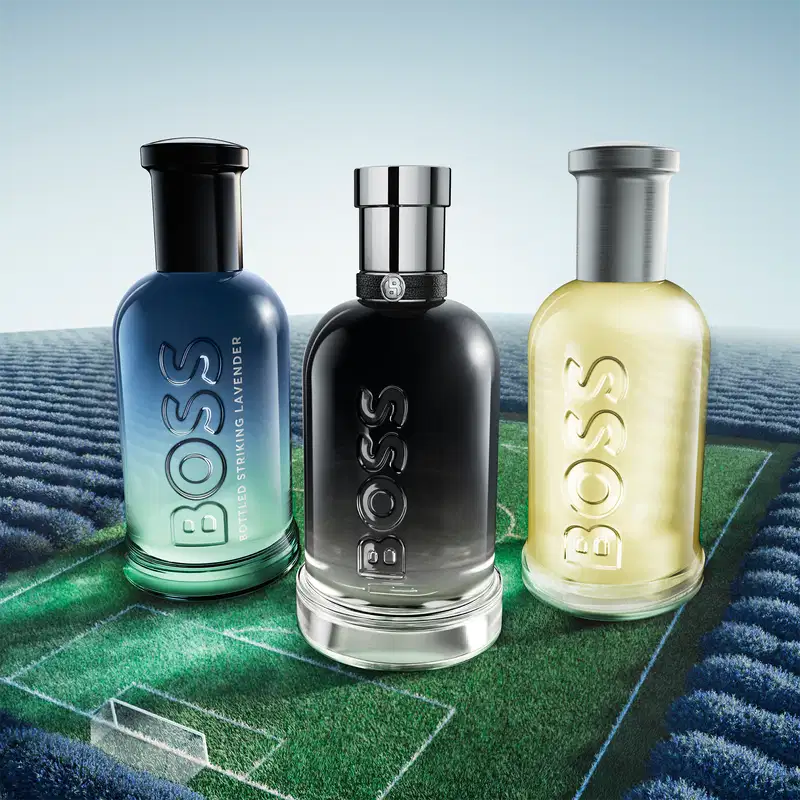 O primeiro é um frasco azul, segundo é um frasco preto e o terceiro é um frasco amarelo, ambos com o texto "Boss". Todos os itens estão dispostos sobre um campo de grama sintética com linhas brancas, sugerindo um campo de futebol.