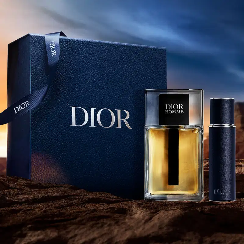 Caixa preta com logotipo Dior em relevo, contendo um frasco de perfume Dior Homme com tampa preta e um frasco de desodorante Dior Homme em fundo preto.