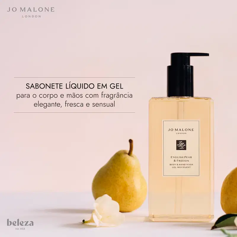 Frasco de item de perfumaria da marca Jo Malone London com rótulo "English Pear & Freesia Body & Hand Wash Gel Moussant" em fundo rosa claro, com uma pera amarela ao lado.