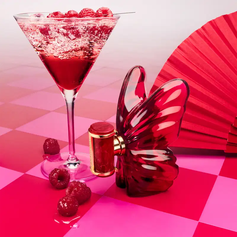 Copo de coquetel vermelho com frutas vermelhas, ao lado do perfume La Bomba Intensa