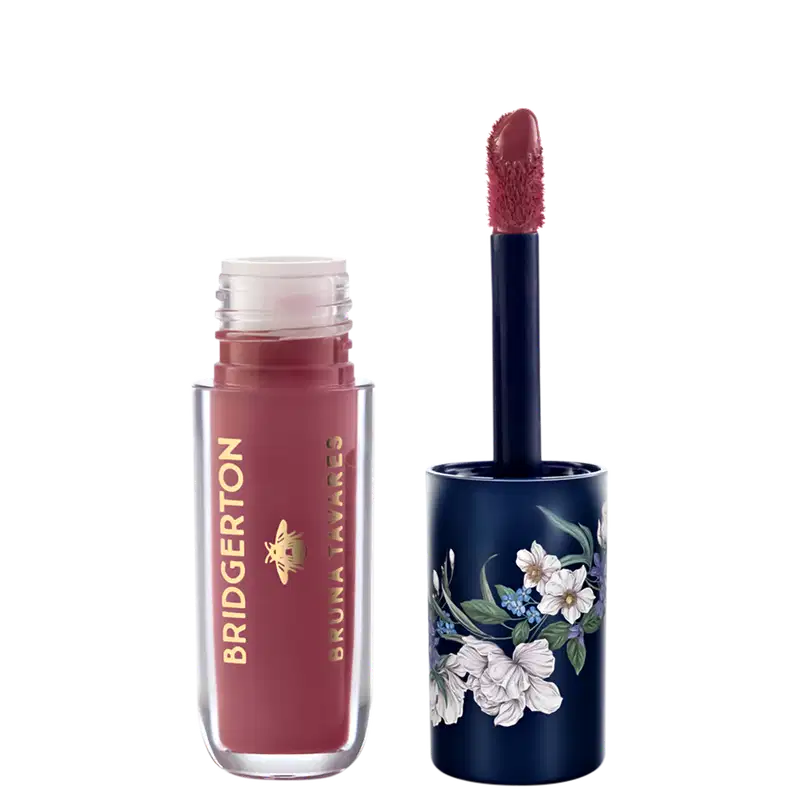 Embalagem de item de maquiagem da marca Bruna Tavares em tom vermelho-rosado com aplicador de espuma, acompanhada de embalagem decorada com flores brancas e azuis em fundo azul-marinho.