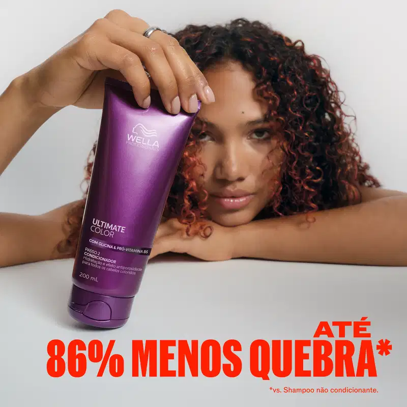 A modelo com cabelos cacheados segura um frasco roxo da linha Ultimate Color da Wella Professionals, destacando o benefício de 86% menos quebra em comparação ao uso de shampoo não condicionante.