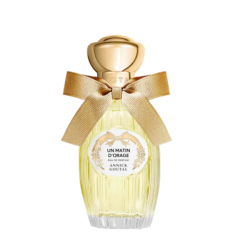 Eau de Parfum Un Matin d'Orage da Annick Goutal em frasco de vidro amarelo claro com tampa dourada esférica, decorado com laço de fita bege e rótulo circular branco com detalhes florais dourados.