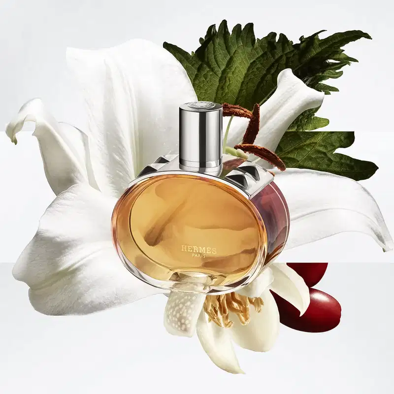 Frasco do Barénia Pleine Fleur, da marca Hermes, junto de lírios e outros ingredientes da fragrância.